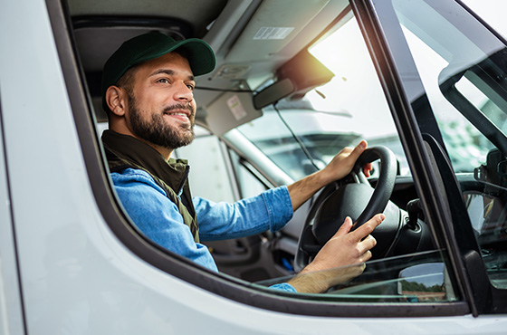 man smiling in the driver's seat of a van with a focus on delivery work wearing a green cap and denim jacket ideal for six delivery services